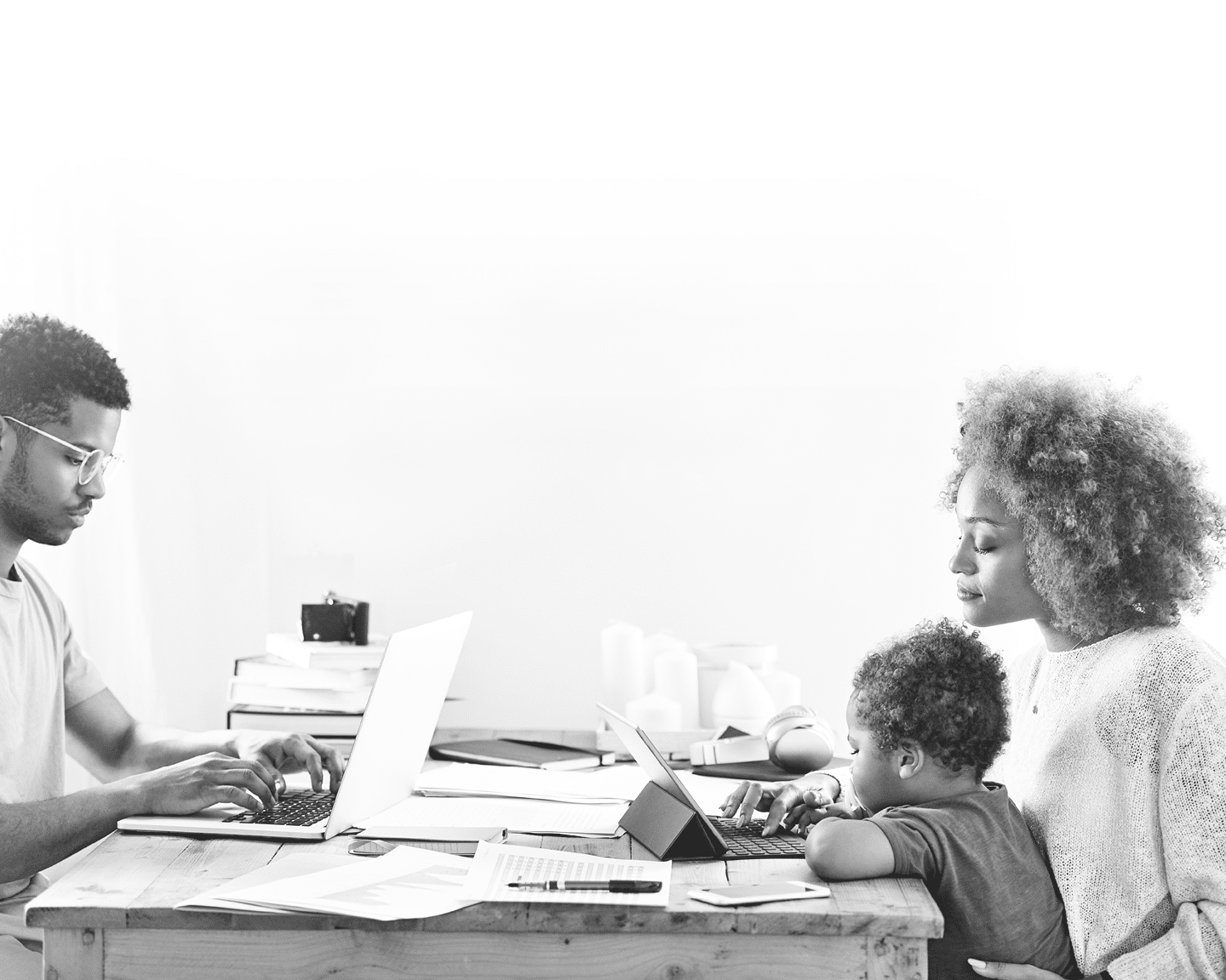 Young man working on laptop  Woman is using digital tablet while sitting with son at table  They are in kitchen at home 