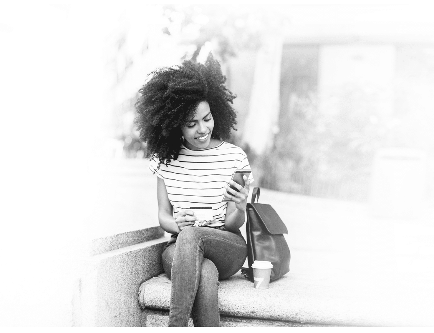 Beautiful, young African - American woman sitting on the street and shopping online 