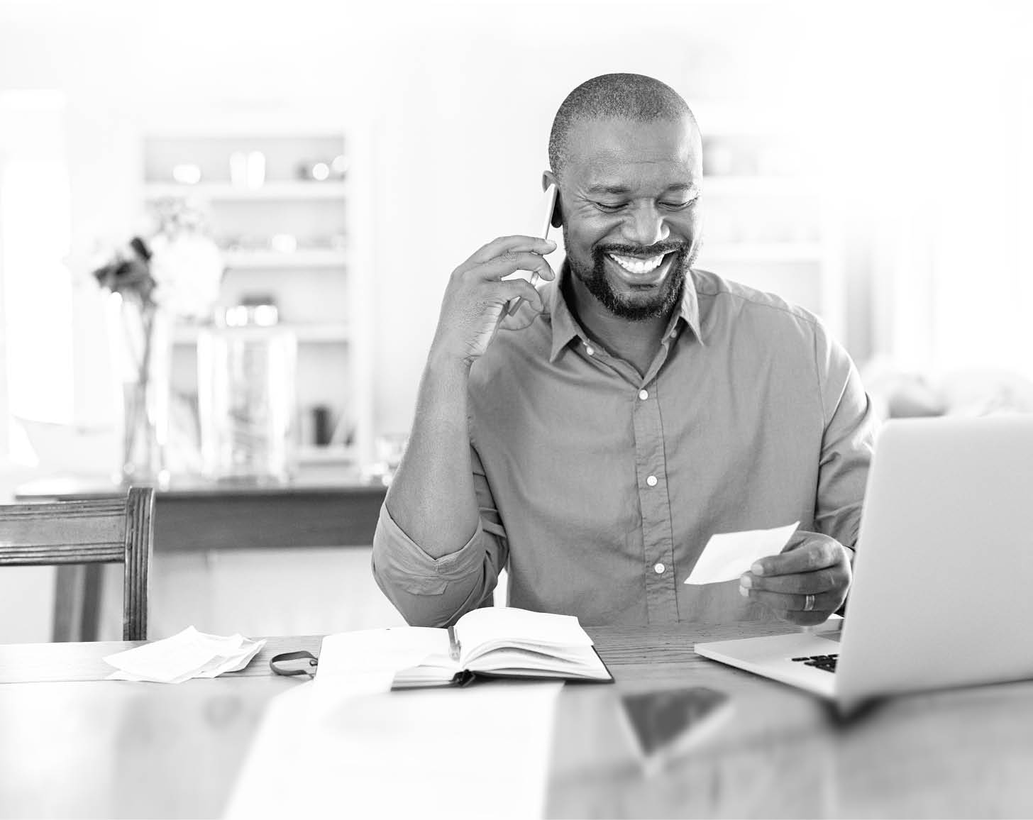 Smiling african man using laptop at home while checking home finance  Happy mature man looking at invoice while talking on phone with bank   Man checking receipt and bill while talking at phone with insurance agent  r